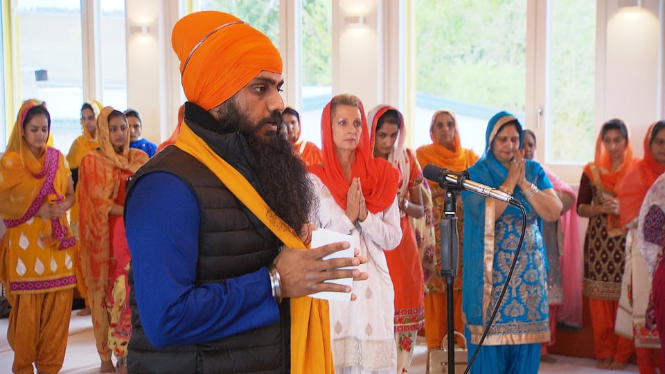 Sikh mit Turban im Vordergrund, dahinter betende Frauen.