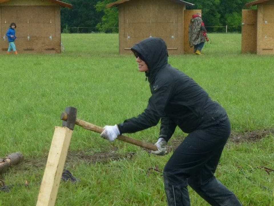 Frau mit Kapuze schlägt mit Hammer auf Holzstück. 