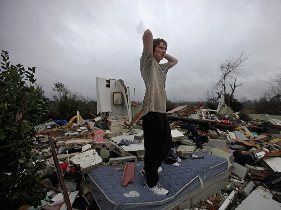 Ein Jugendlicher steht inmitten der Trümmer eines Hauses.