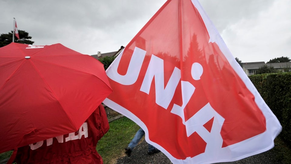 Ein Unia-Gewerkschafter mit Schirm und Fahne.