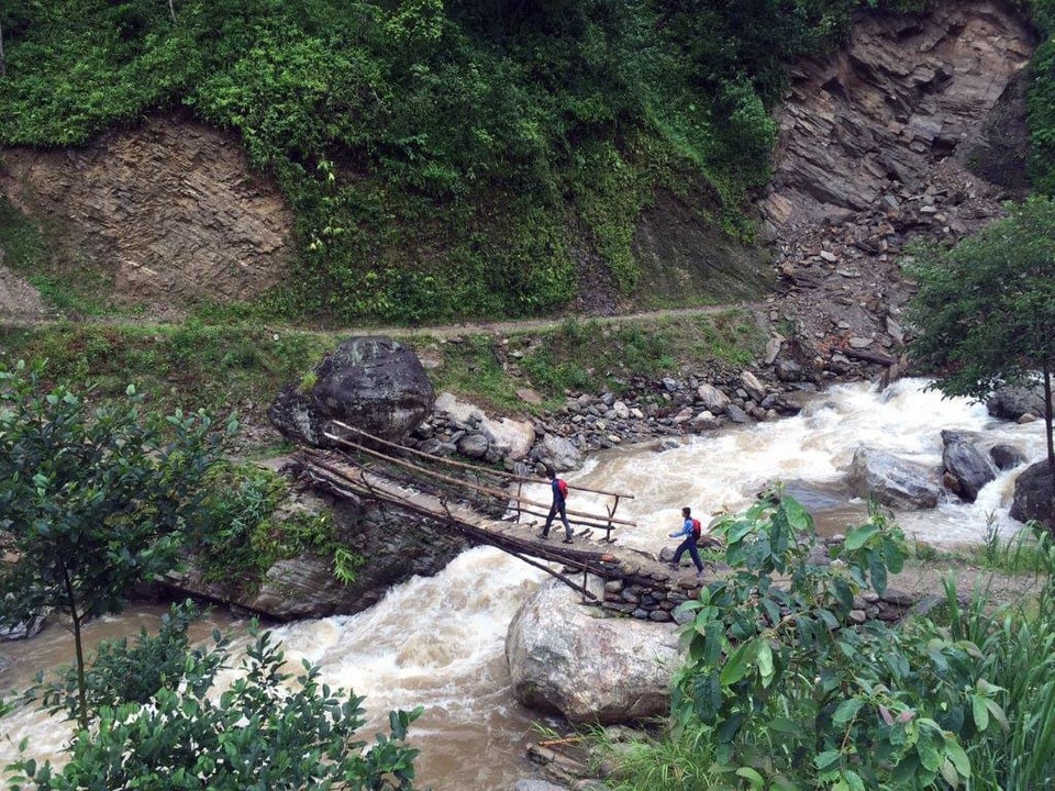 Zwei Schüler gehen über eine kleine Holzbrücke, die über einen reissenden Fluss führt.