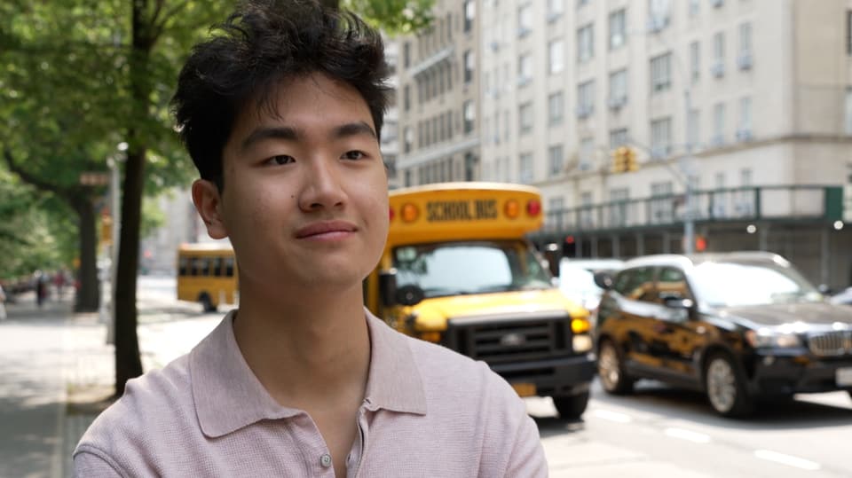 Junger asiatischstämmiger Mann schaut an Kamera vorbei, vor Schulbus