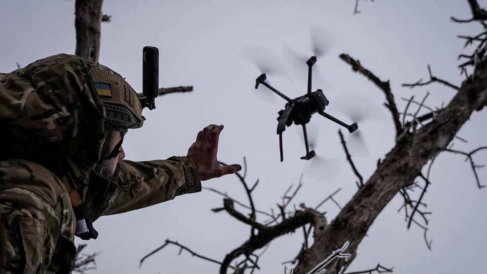 Getarnter Militärangehöriger fingert Drohne zwischen kahlen Bäumen an.