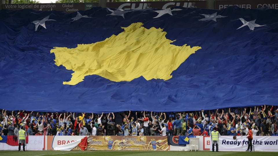 Fussballfans halten eine gigantische Flagge über der Tribüne eines Fussballstadions.