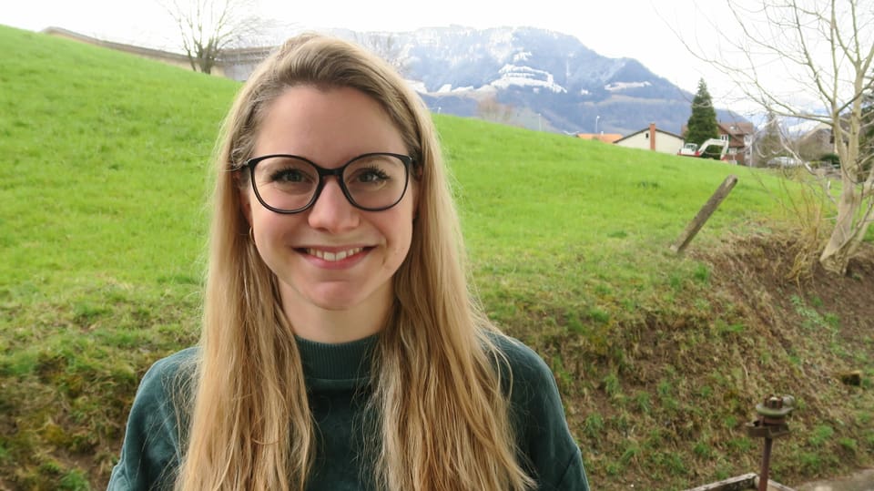 Eine blonde Frau mit Brille vor einer grünen Wiese.