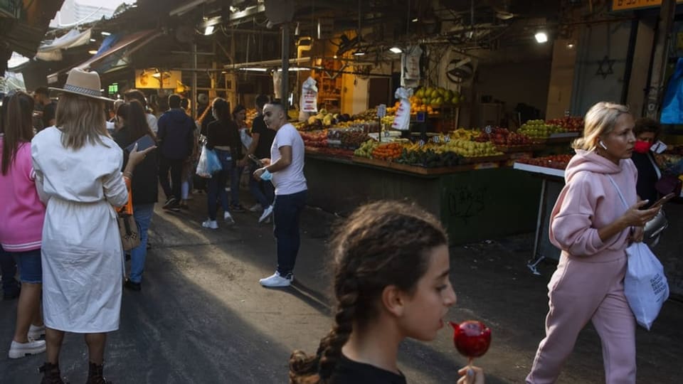 Ein Markt mit vielen Ständen ist zu sehen. Menschen laufen schnell vorbei. 