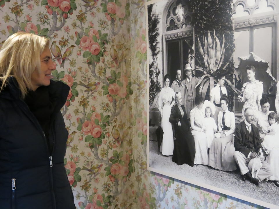 Christina Fankhauser steht neben einem schwarz-weiss-Foto in einem mit Blumen tapezierten Raum.