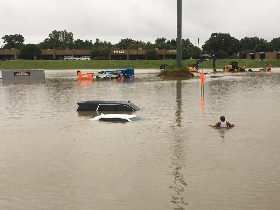 Ein Mann laüft durch Wasser auf zwei im Wasser stehende Autos zu.