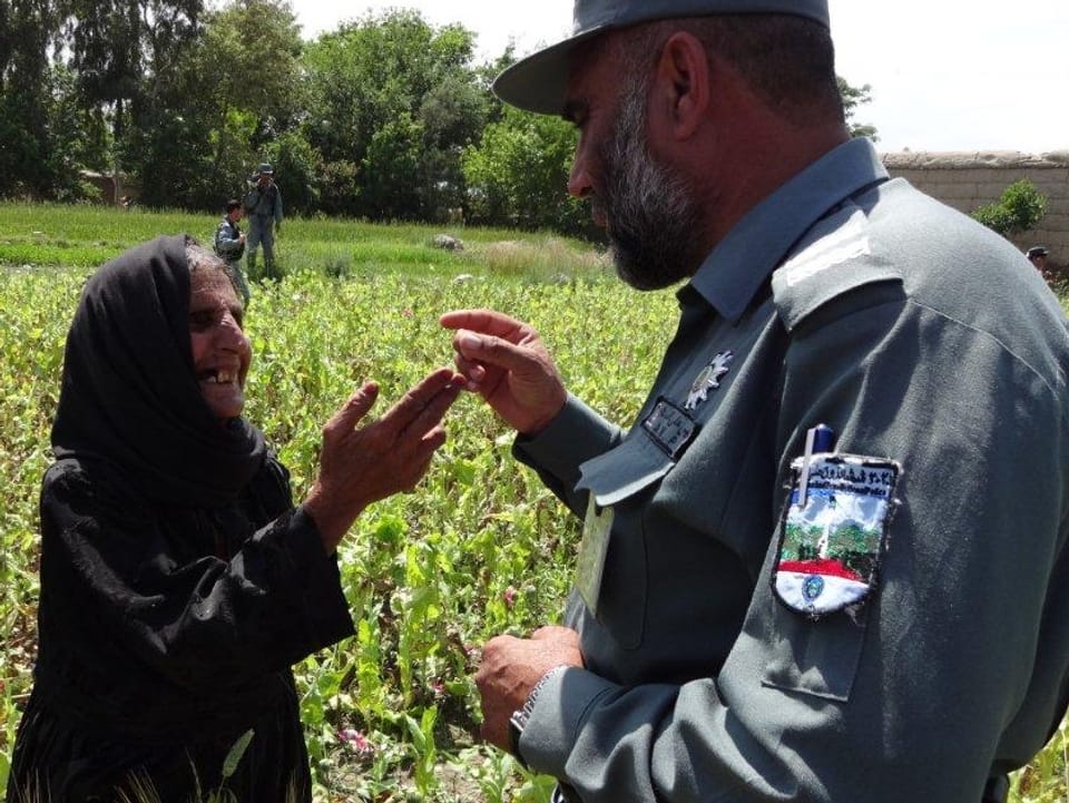 Eine Frau, die in einem Opium-Feld arbeitet, diskutiert mit einem Polizisten.