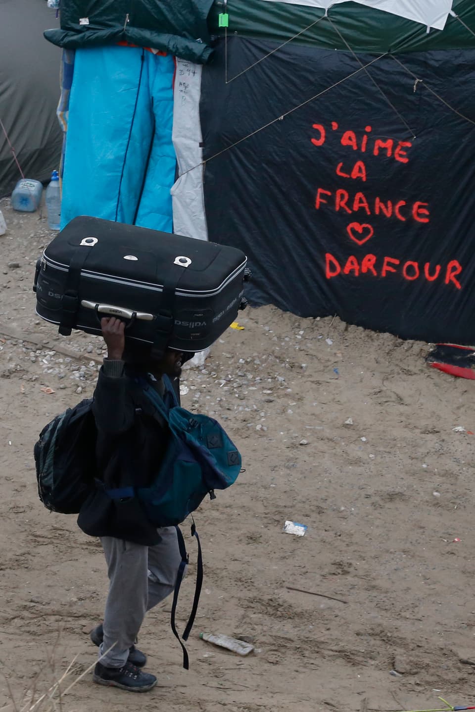 Mann mit Koffer auf dem Kopf neben Grafitti «J'aime la France»