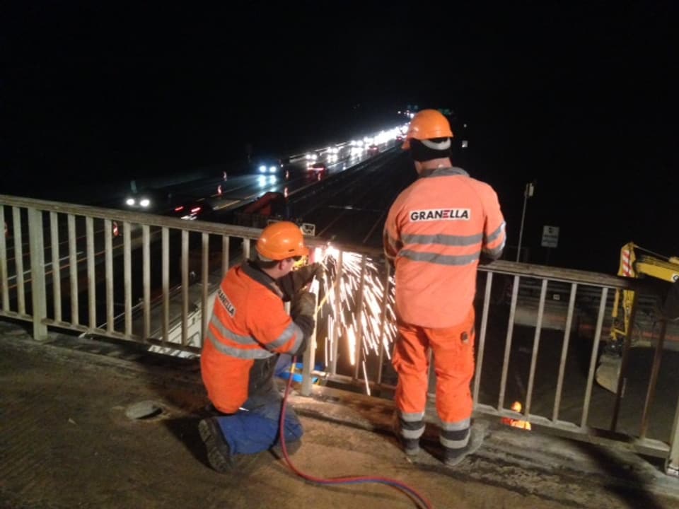 Zwei Arbeiter zerschneiden das Brückengeländer.