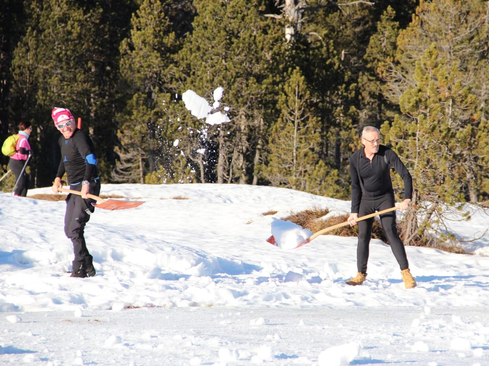 Zwei Männer schaufeln Schnee und richten Langlaufloipen her.