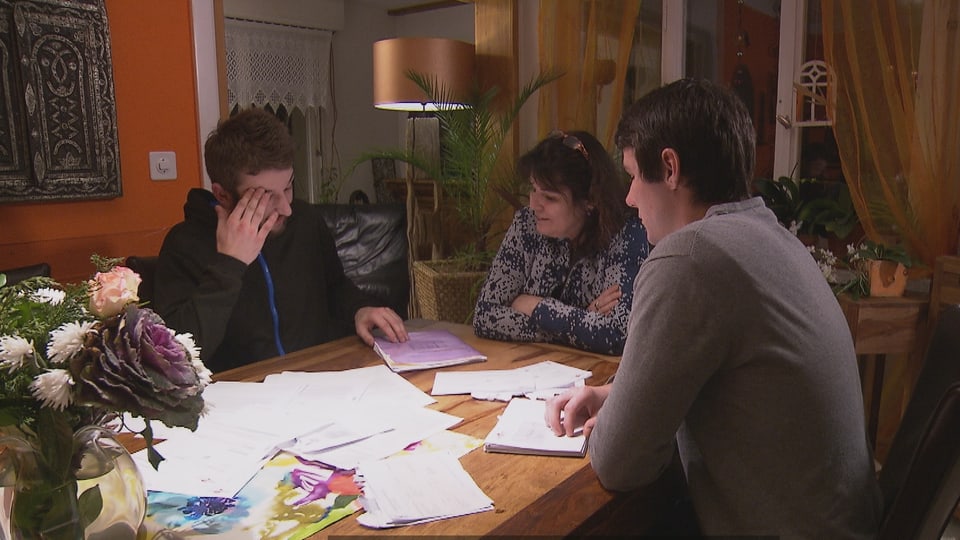 Mutter mit zwei Söhnen sitzen am Tisch und studieren Dokumente.