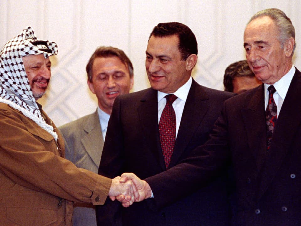 Arafat und Peres geben einander die Hand. Mubarak steht in der Mitte und lächelt Arafat an.