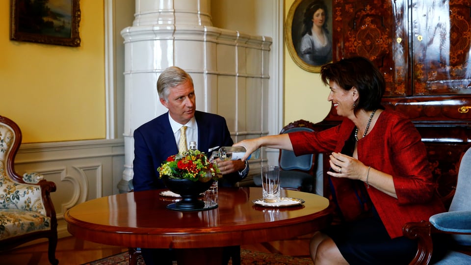 Die Bundespräsidentin bietet dem König ein Glas Wasser an.
