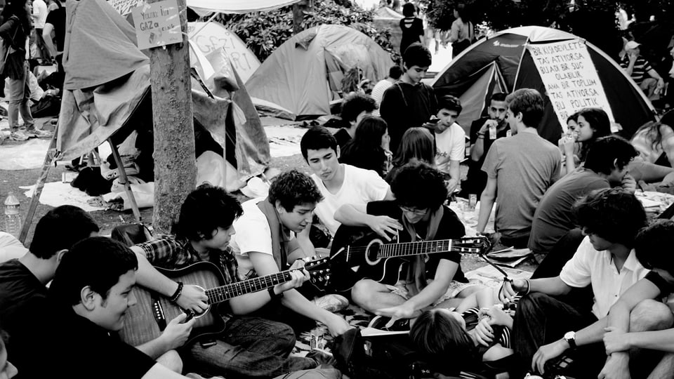 Junge Menschen sitzen auf dem Taksimplatz und spielen Gitarre.