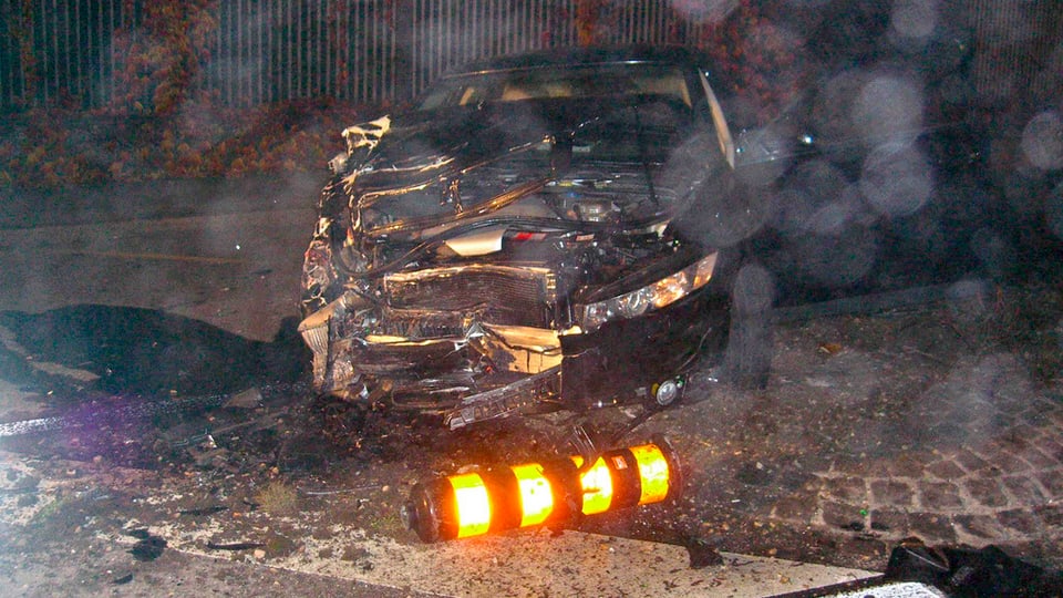 Zerstörtes schwarzes Auto mit umgekippter noch leuchtendem Verkehrszeichen im Vordergrund. 
