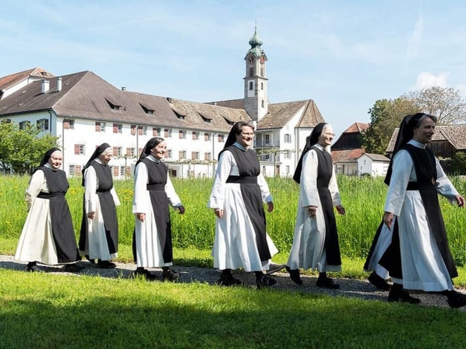 Sechs Nonnen laufen in einer Reihe im Garten vor ihrem Kloster. 