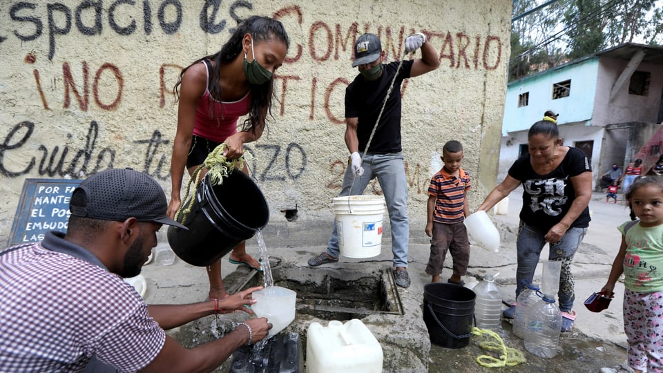 Frauen und Männer füllen an einer Wasserstelle ihre Plastikkanister auf.