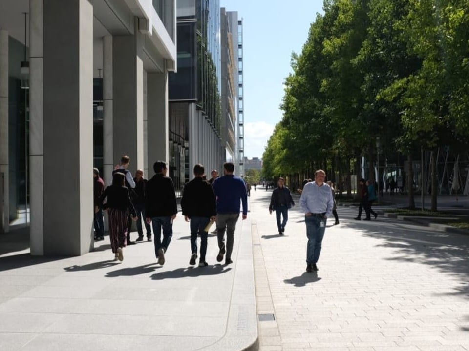 Einige Männer und Frauen in Anzug gehen durch die Hauptstrasse des Novartis-Campus. 