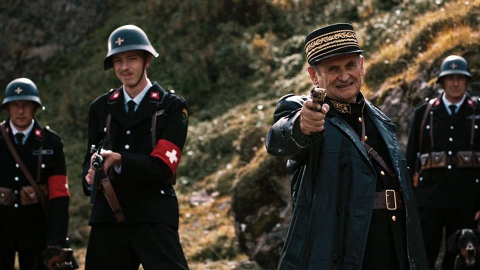 Links zwei Männer in schwarzer Uniform mit Schweizer Kreuz und Helm, rechts ein Mann in Ledermantel, zielt mit Pistole.