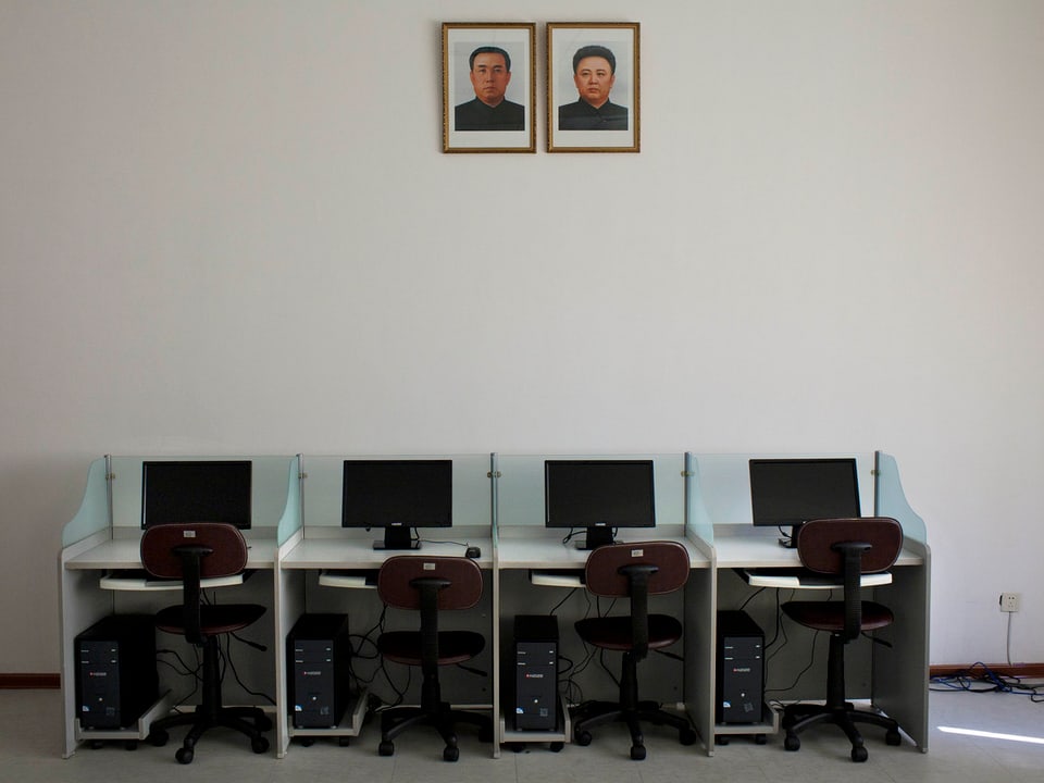 Vier leere Arbeitsplätze: Pulte mit je einem PC und einem Bildschirm und einem spartanischen Bürostuhl.