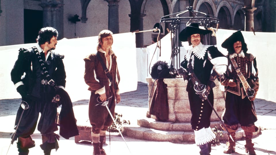 Filmszene aus einem alten Film: Vier Männer mit Degen stehen auf einem Hof.