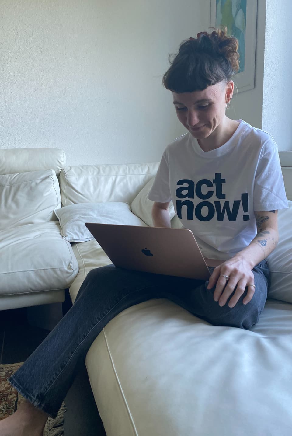 Eine junge Frau mit hochgesteckten Haaren und T-Shirt mit «Act now!»-Aufschrift schaut in einen Laptop.
