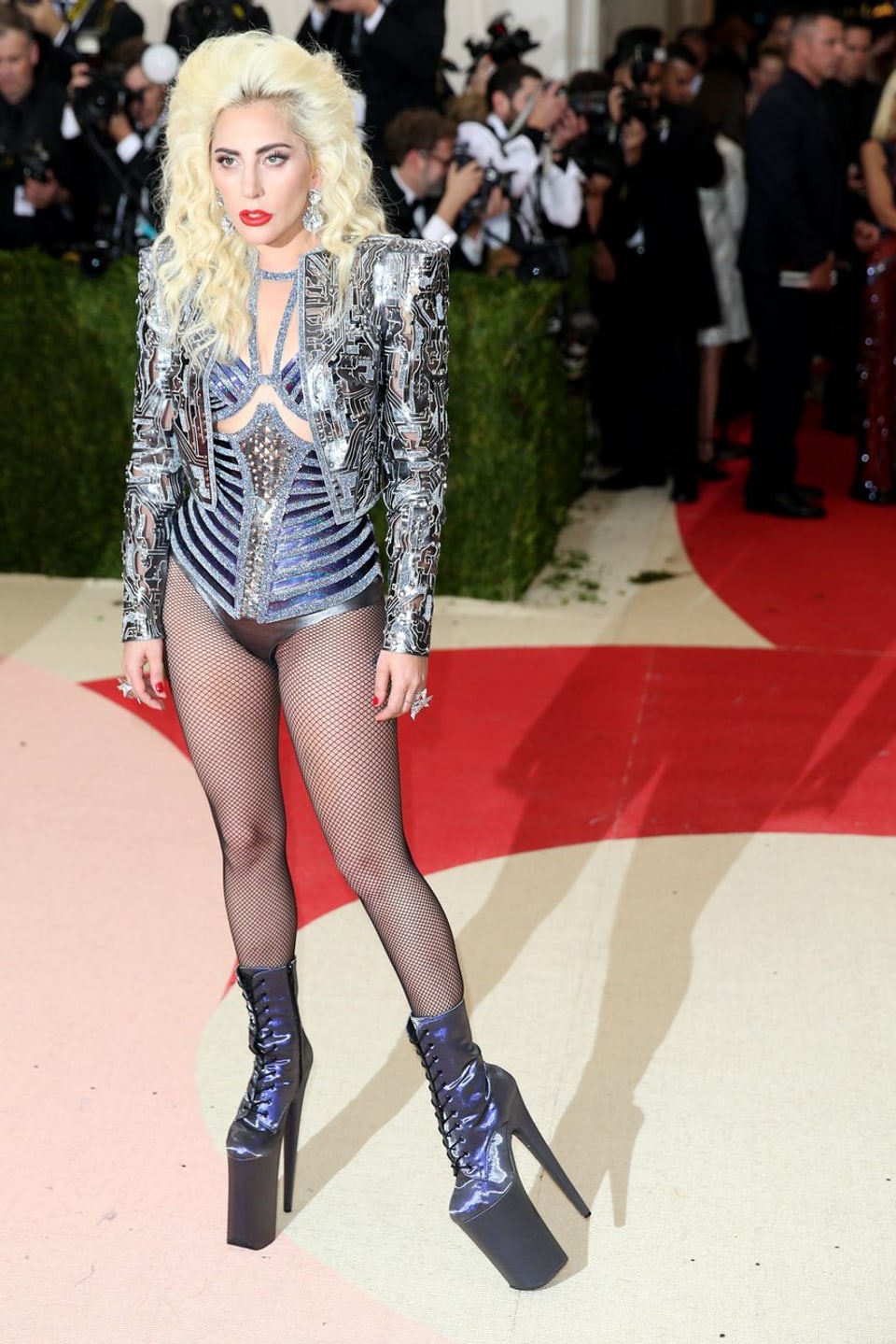 Lady Gaga in einer glitzer Jacke, einer metalischen Korsage und hohen Lederstiefeln. 
