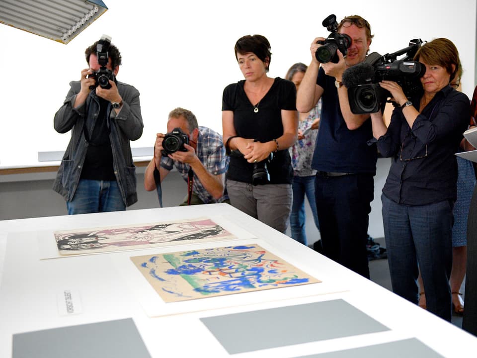 Fotografen und Kamerafrauen sind vor einem gorssen Tisch, auf dem Werke des Gurlitt-Erbes präsentiert werden.