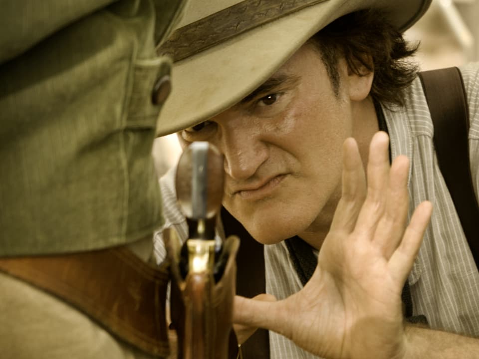 Links Hüfte von Mann mit Revolver, dahinter sieht man den Regisseur. Wirkt sehr konzentriert.