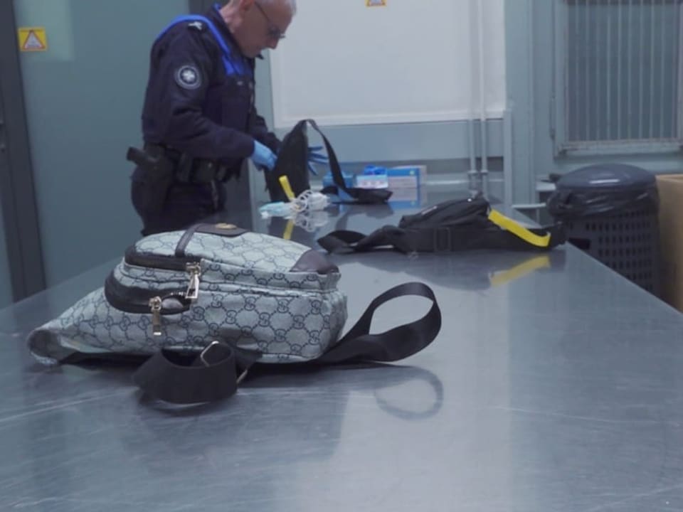Gebäck liegt auf eine Tisch. Ein Grenzschutzbeamter durchkämt einen Sack. 