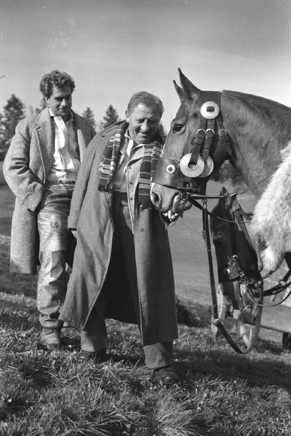 Zwei Männer auf einem Feld im Frühlingsmantel. Der ältere der zwei streichelt ein Pferd.