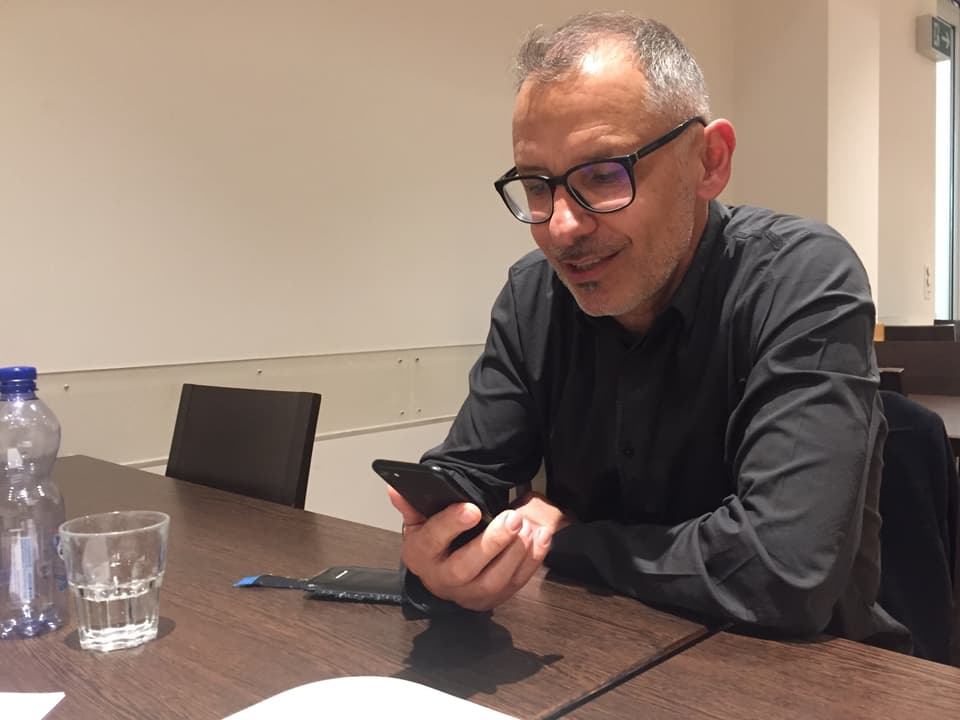 Mann mit Brille sitzt am Tisch und schaut auf sein Smartphone