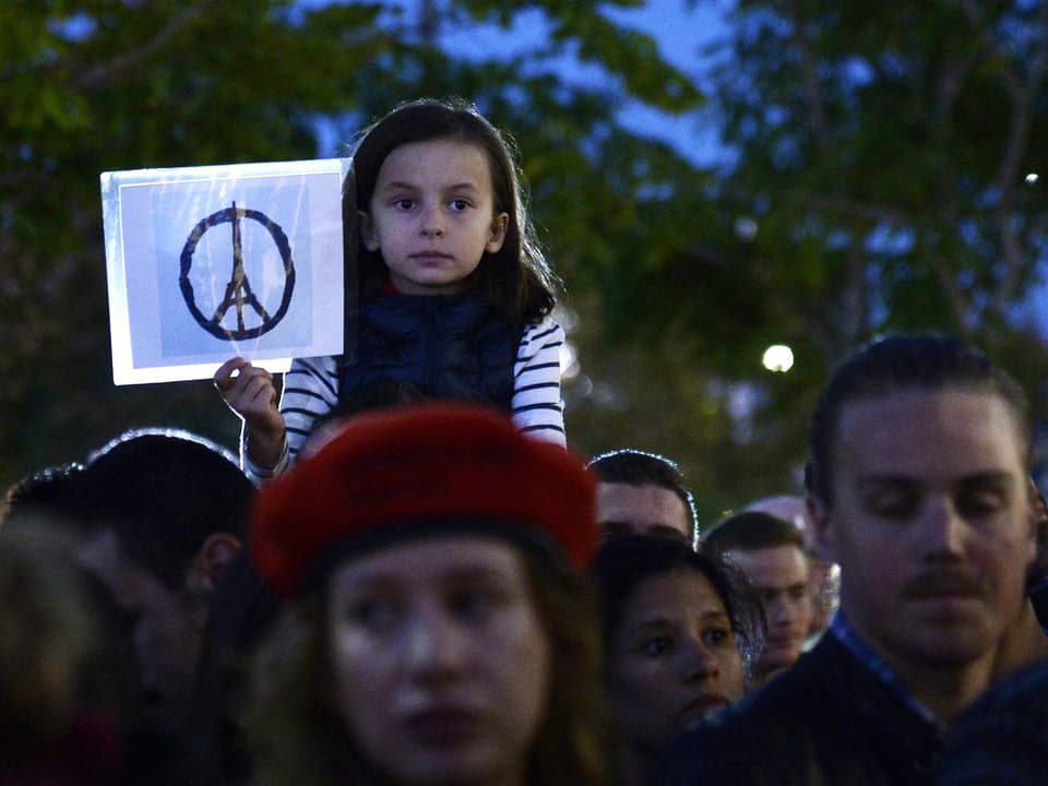 Ein Mädchen in einer Menschenmenge hält ein gezeichnetes Peace-Zeichen in der Hand.