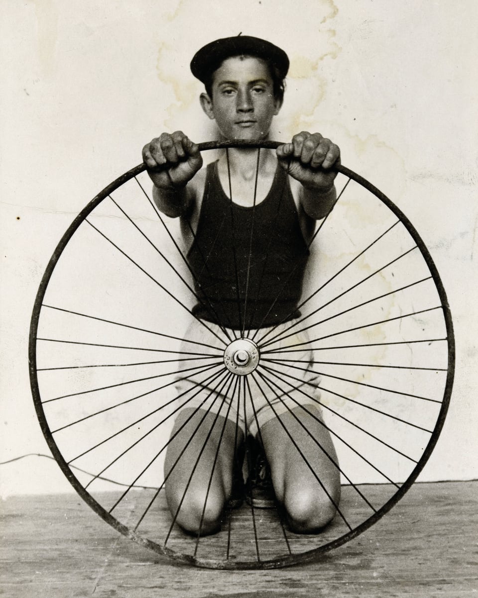 Ein Junge mit Baskenmütze kniet hinter einem Rad.