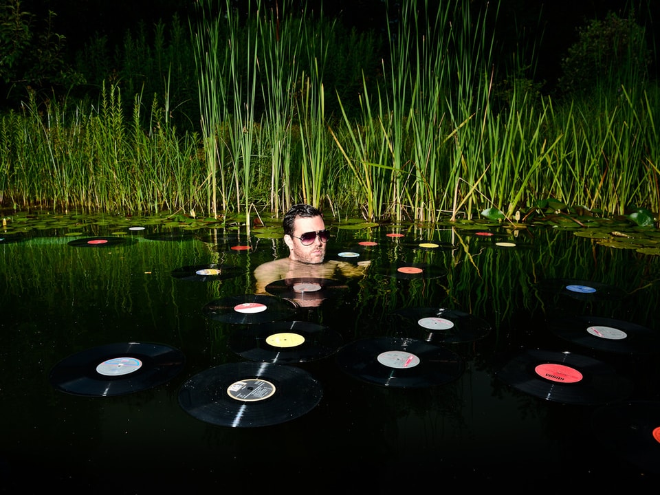 Ein Mann badet in einem See voller Vinylplatten. 
