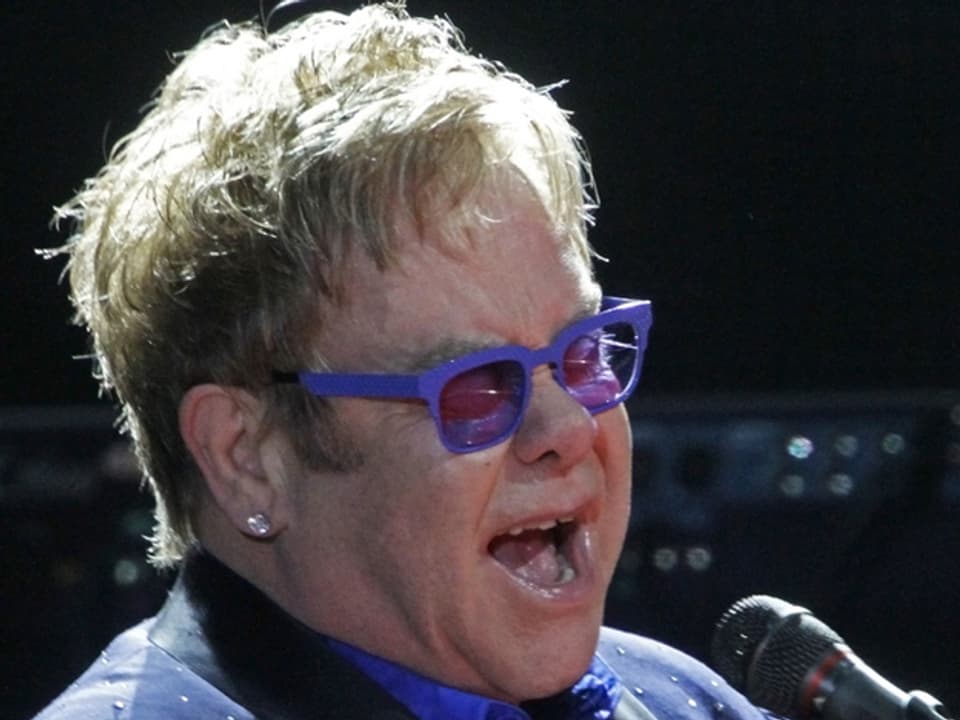 Elton John singend mit violetter Brille.
