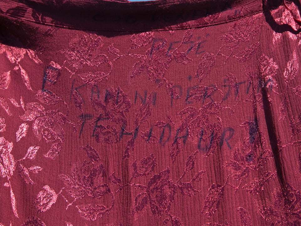 Ausschnitt aus einem weinroten Kleid, Aufschrift.