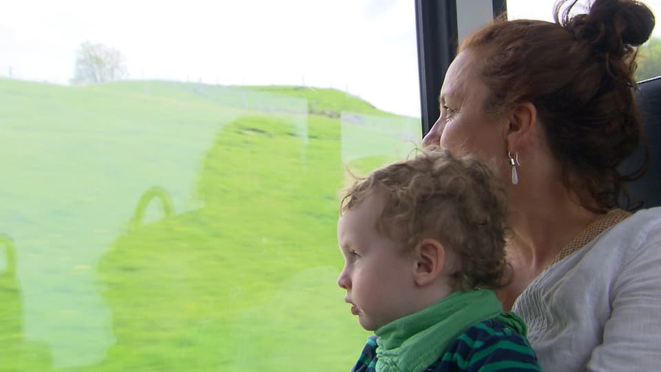 Enkel sitzt im Zug auf dem Schoss der Grossmutter. Beide schauen aus dem Fenster.