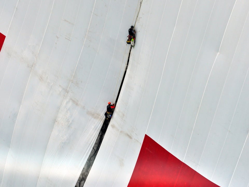 Mit Seilen und Spannsets flicken die Höhenarbeiter die Schweizerfahne am Berg.