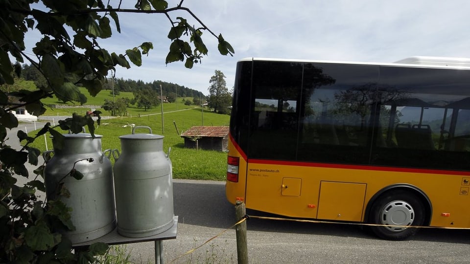 Gelbes Postauto vor Milchkannen im Grünen. 