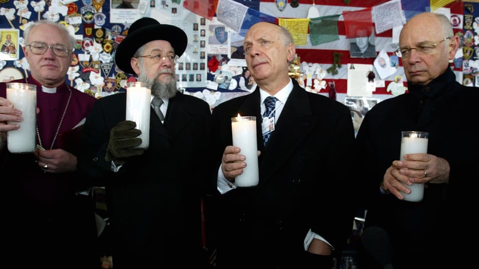 Vier Männer halten je eine Kerze in der Hand.
