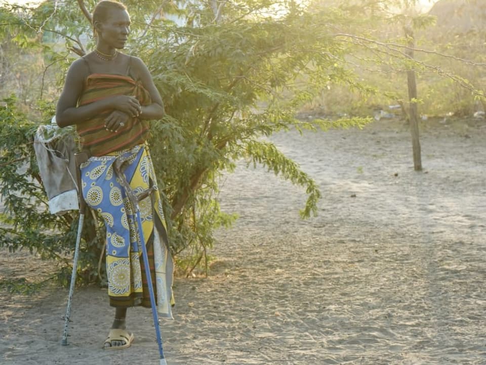 Eine Frau mit einem Bein steht mit Krücken in der Wüste.