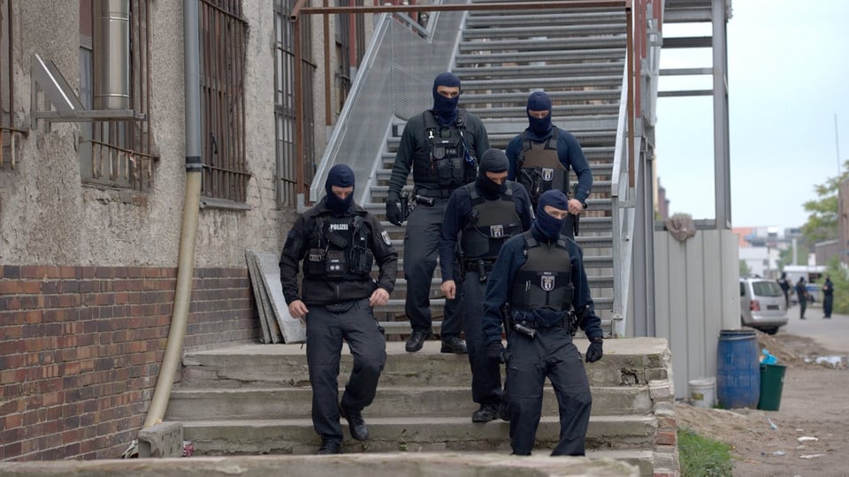 Polizisten mit Masken verlassen ein Gebäude auf einer Treppe.
