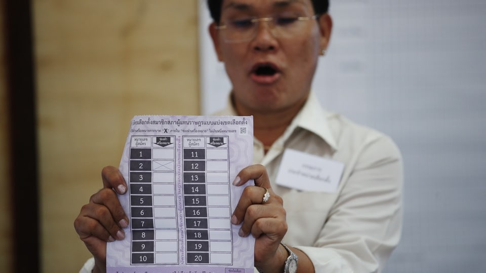 Ein thailändischer Wahlhelfer hält einen Stimmzettel hoch