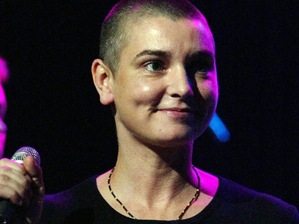 Sinead O'Connor on stage holding a microphone in her right hand. 