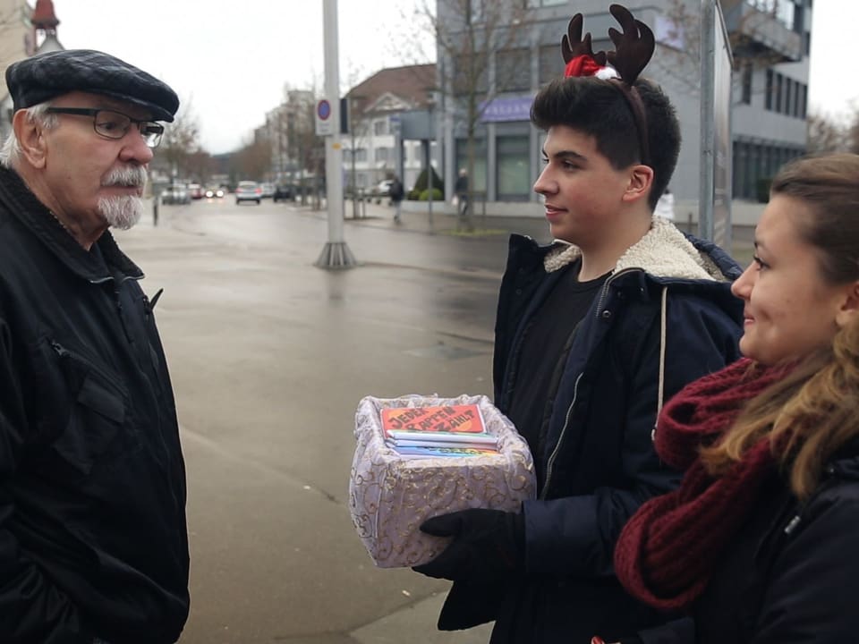 Zwei Jugendliche verkaufen einem älteren Herrn auf der Strasse Schokolade.