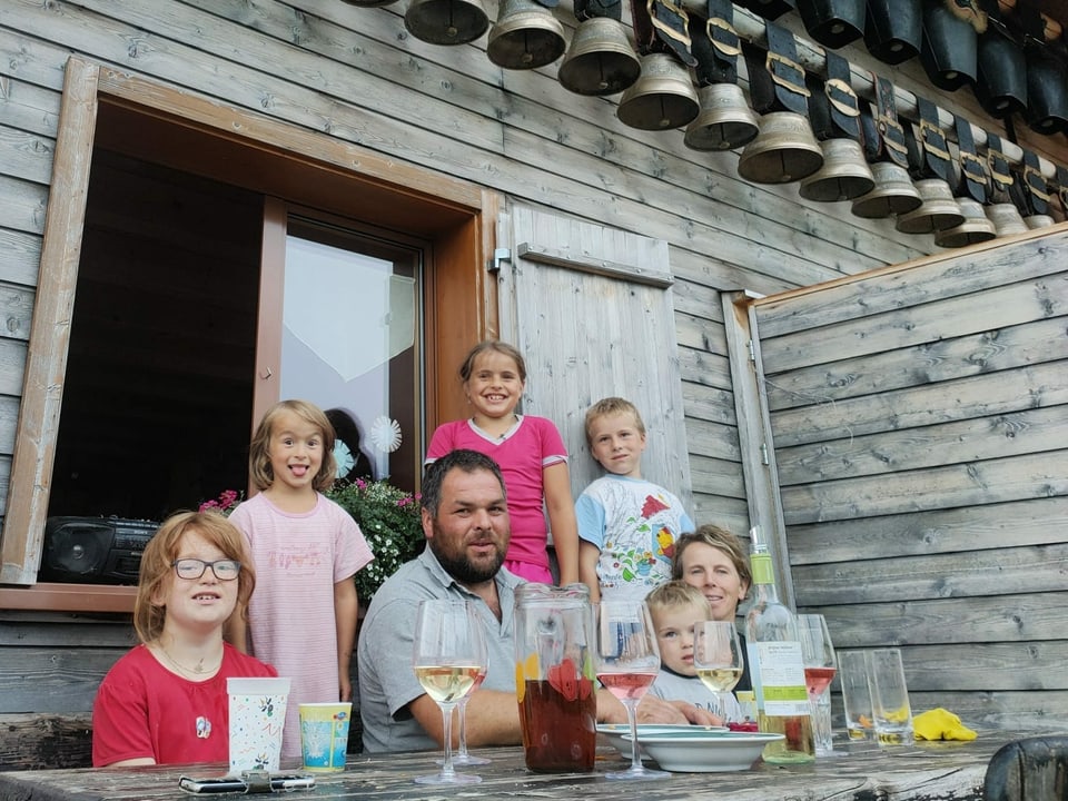 Eine Familie mit fünf Kindern sitzt vor einer Alphütte.