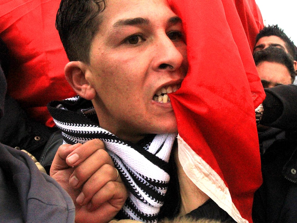 Ein junger Mann beisst in die tunesische Nationalflagge.